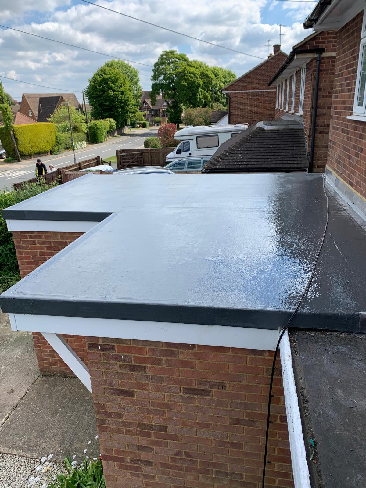 Finished grey GRP fibreglass garage roof with black drip trims, on a brick garage beside the house