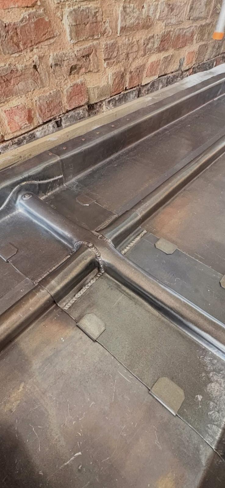 Lead flat roof with welded rolls meeting at a T-junction, dressed up to an old brick wall