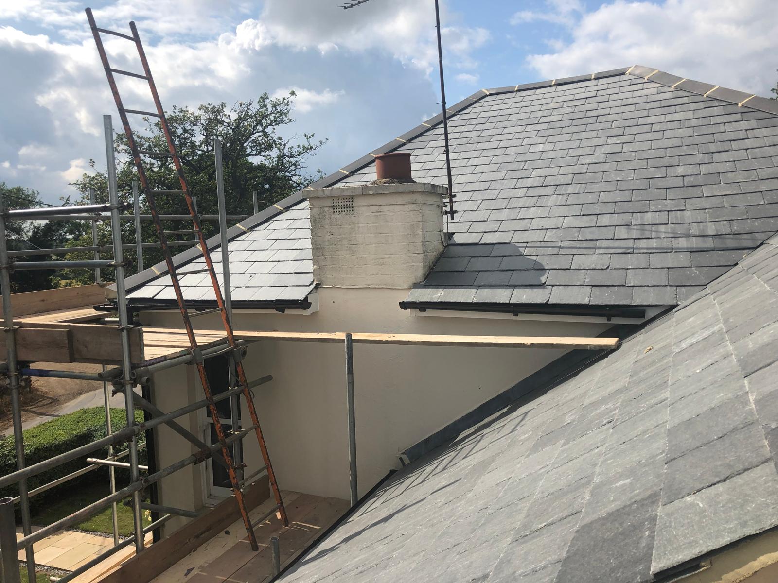 New blue-grey slate roof with a rendered chimney stack and lead soakers, seen from the scaffold